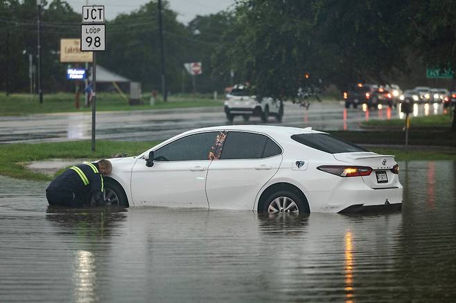 13일 텍사스 잉그램에서 대형 견인차 기사가 도로에 물에 잠긴 자동차에 케이블을 연결하려 하고 있다.[AFP]