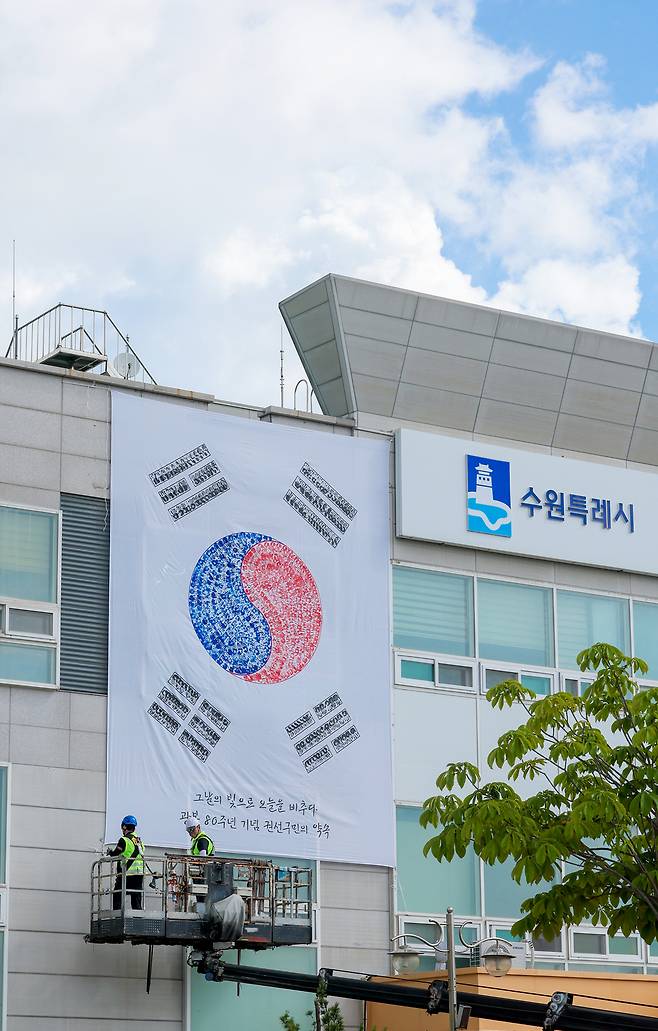 ▲ 제80주년 광복절을 앞두고 22일 오전 수원시 권선구청 외벽에 관계자들이 손도장으로 만든 대형 태극기를 설치하고 있다. /전광현 기자 maggie@incheonilbo.com