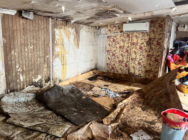 지난 17일부터 계속된 호우로 김춘식씨 비닐하우스 바로 옆에 붙어있던 작업공간은 완전히 망가져버렸다. 사진은 22일 오전 봉사자들이 토사가 묻은 장판을 걷어내고 있는 모습. /사진=민수정 기자.