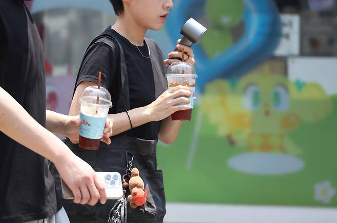 28일 대구에 폭염경보(군위 제외)가 내려진 가운데 중구 동성로에서 시민들이 아이스 아메리카노와 휴대용 선풍기로 더위를 식히며 이동하고 있다. [사진 출처 = 연합뉴스]