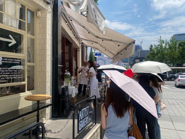 무더위가 계속된 이달 24일 서울 종로구에 있는 한 유명 베이커리집 앞에서 고객들이 양산을 쓴 채 입장을 기다리고 있다. 이 곳은 소비쿠폰 사용이 불가능한 곳이다. 사진=조수연 인턴기자