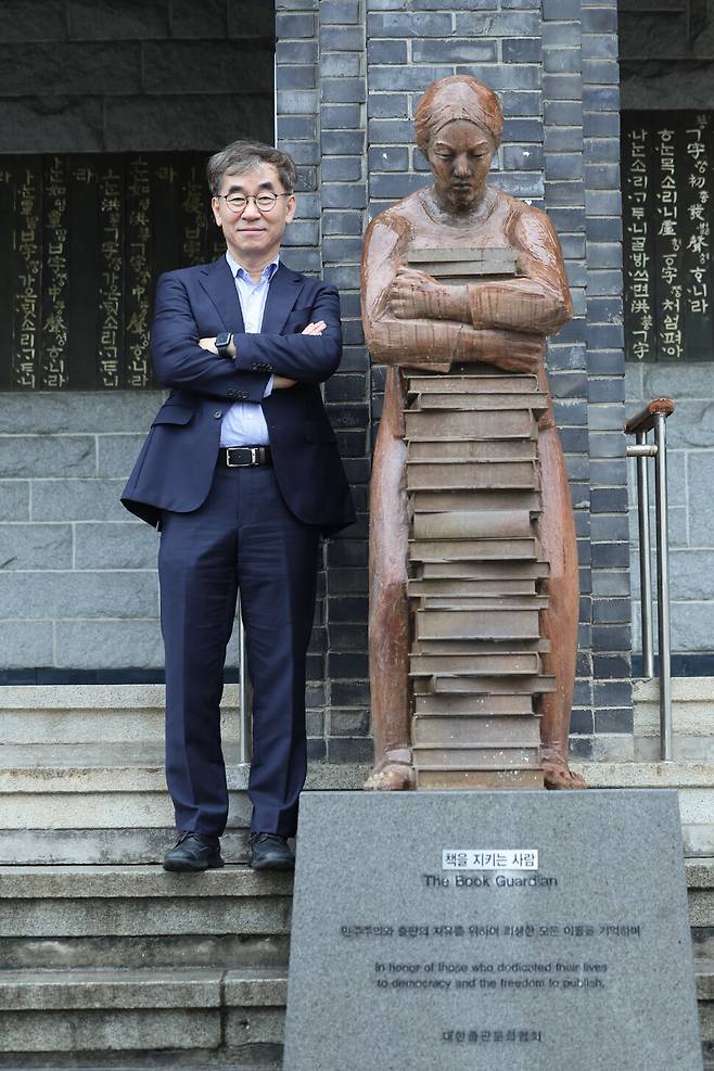 윤철호 대한출판문화협회 회장이 지난 16일 오후 서울 종로구 출판문화회관 들머리에 있는 조형물 ‘책을 지키는 사람’ 옆에 섰다. 1980~90년대, 출판의 자유와 민주화를 위해 헌신한 출판인·작가·번역가·서점인·제작자를 새긴 명판(기둥 측면)과 함께 지난해 12월 조형물이 세워졌다. 김영원 기자 forever@hani.co.kr