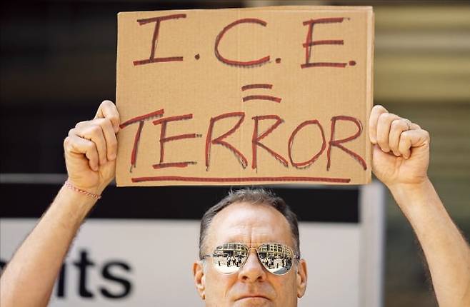 < “이민 단속은 테러” > 미국 시민이 24일(현지시간) 뉴욕시의 연방 청사 건물 앞에서 ‘ICE(이민세관단속국)는 테러’라고 적힌 손팻말을 들고 서 있다.   /UPI연합뉴스