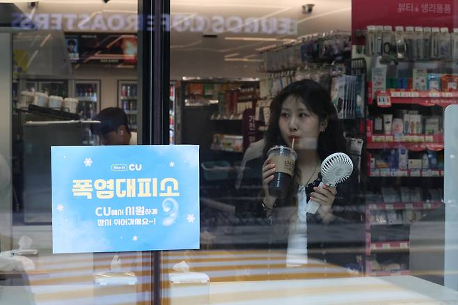 A woman stands inside a CU convenience store in Seoul, where a sign indicates the store is serving as a cooling shelter, Thursday. (Yonhap)