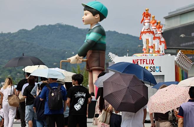 서울 종로구 광화문광장에 마련된 넷플릭스 '오징어 게임' 체험존에 지난 4일 관광객들이 무더위에도 불구하고 양산을 쓰고 대기하고 있다. 뉴스1