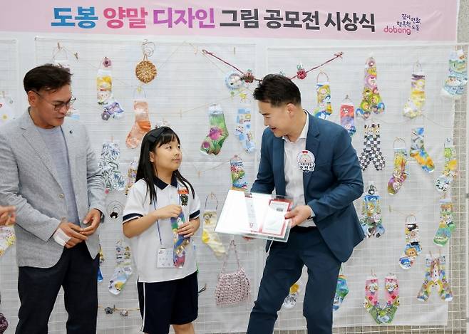 오언석(오른쪽) 서울 도봉구청장이 지난 14일 구청 선인봉홀에서 열린 ‘제3회 도봉 양말 디자인 그림 공모전’ 시상식에서 대상 수상자 이서유(가운데)양에게 상패를 건네고 있다. 도봉구 제공