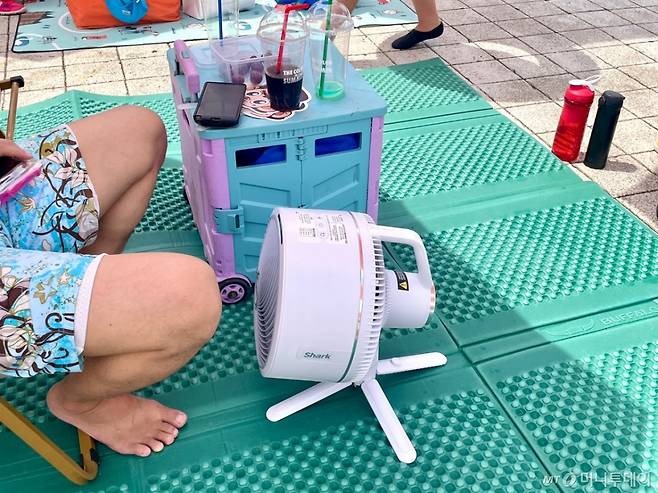 30일 오전 서울 광진구 뚝섬한강공원 수영장에서 한 시민이 직접 챙겨온 선풍기 바람을 쐬고 있다. /사진=이현수 기자.