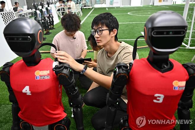 작전지시? 휴머노이드 로봇 종합 운동회(14∼17일)4일 베이징에서 열린 휴머노이드 로봇 축구 시범경기에서 한 학생이 로봇 선수들을 살피고 있다. [AFP=연합뉴스]