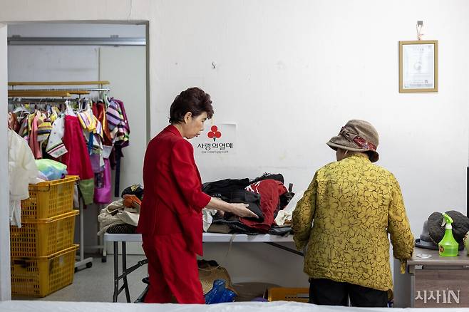 김미선 원장이 동네 사람들에게 받은 구제 물품 중 모자 하나를 손님에게 1000원에 팔고 있다. 수익금은 사랑의 열매에 전액 기부한다. ⓒ시사IN 박미소
