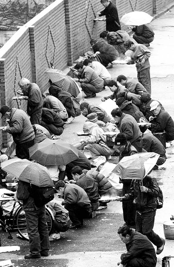 당시 서울 용산역에서 비가 내리는 가운데 실직자들이 무료 급식을 먹고 있다. [중앙포토]