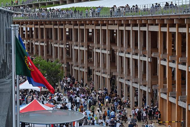 세계 최대 목조건축물인 일본 오사카 엑스포 ‘그랜드 링’ 근처에 관람객들이 모여있다. 이 건축물은 못 하나 없이 ‘기둥’과 ‘보’를 연결하는 일본의 전통 목조건축 기법으로 건축됐다. (사진=AFP)