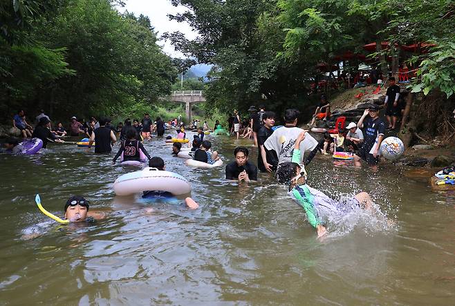 2025년 8월 첫째 주말인 2일 경기도 양평군 옥천면 신복천에서 오윤상(앞줄 오른쪽)군이 물속에서 공중제비를 돌며 공을 차고 있다. 뒤쪽에서 시민들이 아이들과 어울려 놀고 있다.