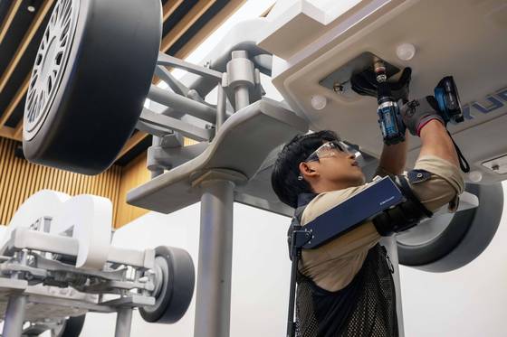 A worker secures a bolt to the underside of a vehicle while wearing the X-ble Shoulder. [HYUNDAI MOTOR AND KIA ROBOTICS LAB]