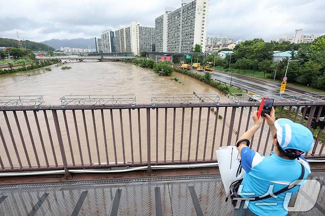 서울 동북·서북권에 호우경보가 발령된 13일 서울 노원구 월계동에서 한 시민이 집중호우에 불어난 중랑천을 스마트폰 카메라에 담고 있다. 2025.8.13/뉴스1 ⓒ News1 민경석 기자