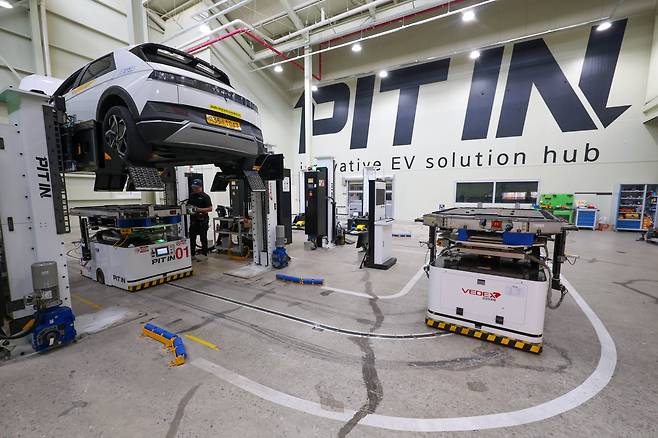 지난달 29일 경기도 안양시 '피트인'에 전기 택시 아이오닉 5가 배터리 교체를 위해 리프트에 올라가 있다. 로봇 한 대(우측)가 다 쓴 배터리를 싣고 나오고 있고, 다른 로봇은 차량 아래쪽에서 완전히 충전된 배터리를 다시 장착하고 있다. /안양=장련성 기자