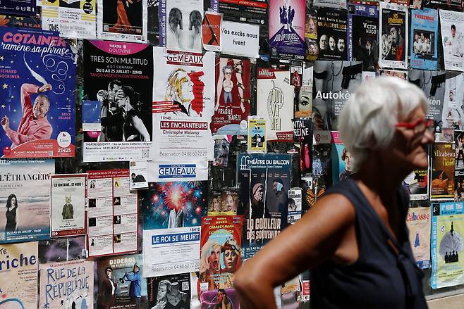 A woman stands in front of a wall covered with posters advertising plays during the Festival d'Avignon in Avignon, France, July 16. [REUTERS/YONHAP]