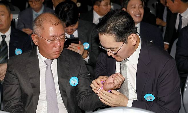 15일 서울 세종대로 광화문광장에서 열린 제21대 대통령 국민임명식 '광복 80년, 국민주권으로 미래를 세우다' 행사에서 이재용 삼성전자 회장이 정의선 현대차그룹 회장에게 팔찌를 채워주고 있다. 연합뉴스