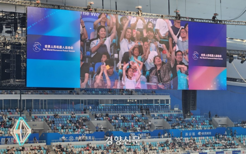 16일 국립스피드스케이트경기장에서 열리는 로봇올림픽을 관람하던 관중들이 중계 카메라가 비추자 팔로 하트 모양을 만들어 보이고 있다. 베이징 | 박은하 특파원