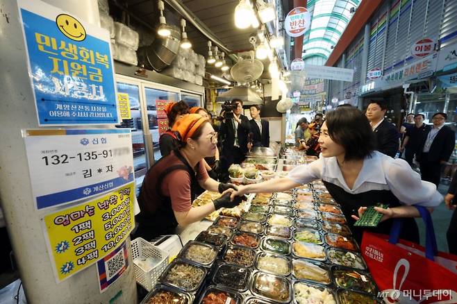 [인천=뉴시스] 고범준 기자 = 이재명 대통령 부인 김혜경 여사가 25일 인천 계양산전통시장을 찾아 민생회복 소비쿠폰을 이용해 음식을 구매한 뒤 상인과 인사하고 있다. 2025.07.25. bjko@newsis.com /사진=고범준