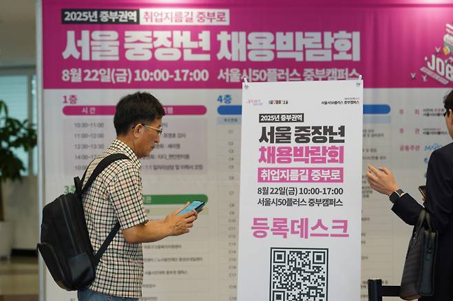 22일 서울 마포구 서울시50플러스 중부캠퍼스에서 열린 ‘2025년 서울 중부권역 중장년 채용박람회’를 찾은 한 구직자가 현장 등록을 위해 배너를 살피고 있다. 서울시50플러스재단 제공