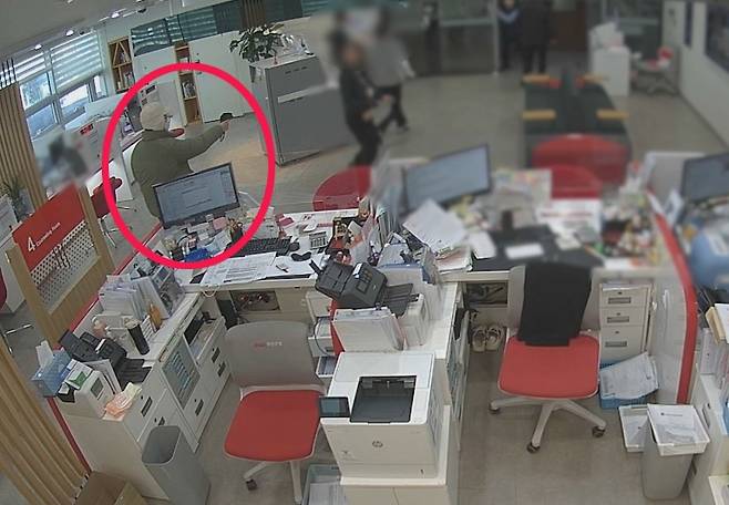 A man threatens bank employees with a toy squirt gun wrapped in a plastic bag to resemble a real firearm in Busan on Feb. 10. [YONHAP]
