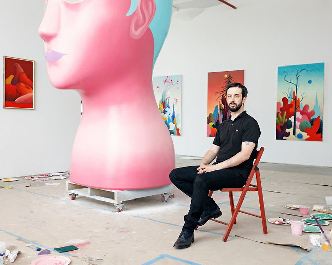 작업실에서 풍경화와 조각 앞에서 앉은 니컬러스 파티. [Nicolas Party]