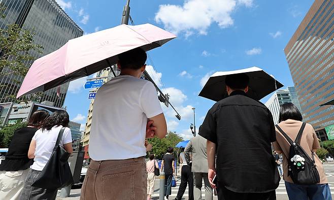 더위가 그친다는 절기상 처서를 하루 앞두고 찜통더위가 이어진 지난 22일 서울 종로구 광화문 네거리에서 양산을 쓴 시민들이 신호를 기다리고 있다. 뉴시스