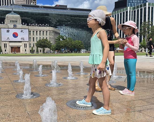 서울광장 분수 주위에서 한 엄마가 아이들에게 물안경과 모자를 씌우고 있다.