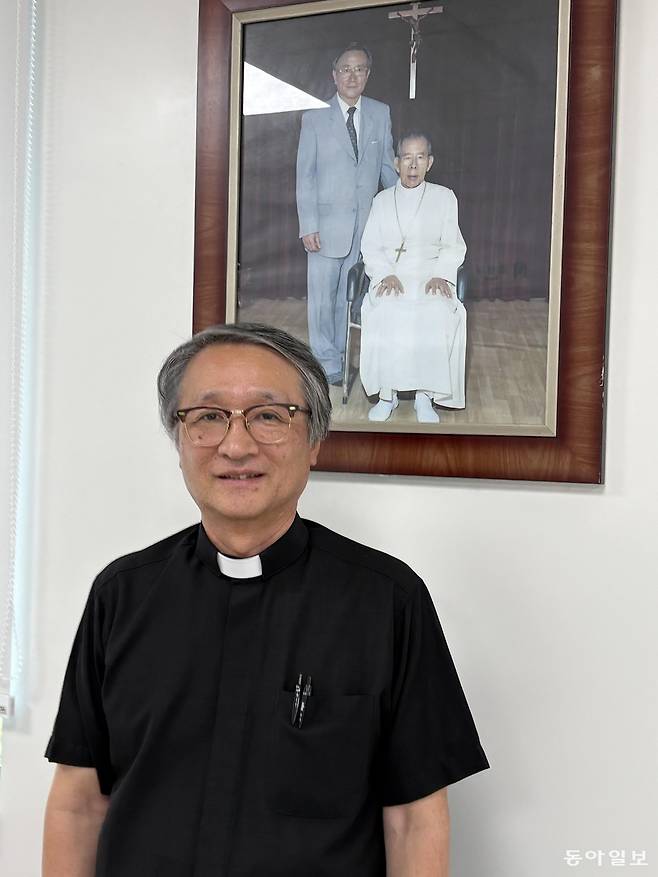 홍근표 요셉나눔재단 사무총장 신부가 김수환 추기경과 선우경식 1대 원장의 사진을 배경으로 포즈를 취했다. 그는 스스로를 돌보기 힘든  환자들을 발견하고 돕기 위해 방문의료팀이 환자를 찾아가는 의료시스템을 적극 추진하고 있다.  서영아 기자 sya@donga.com