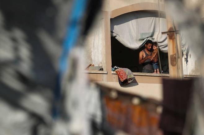 한 팔레스타인 남성이 8일(현지시간) 피난민들을 위한 건물 창가에 아이와 함께 서서 밤새 이스라엘군이 가자 시티의 난민촌을 공격한 현장을 내려다보고 있다. /로이터=뉴스1