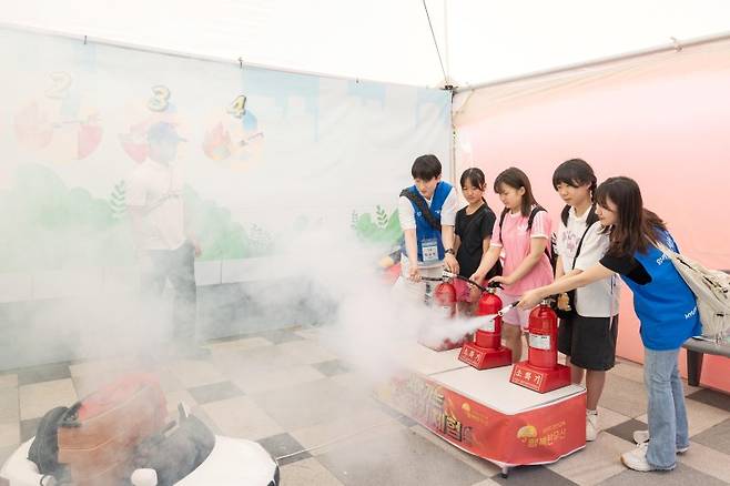 현대글로비스가 지난 6월 서울대공원 인근에 마련한 '물류 이동 안전 체험존'에서 임직원과 어린이들이 소화기를 이용한 가상 화재 진압 체험을 하고 있다.