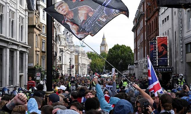 영국 극우 활동가 토미 로빈슨(본명 스티븐 악슬리레넌) 지지자가 13일(현지시각) 런던에서 도널드 트럼프 미국 대통령을 람보로 묘사한 깃발을 흔들고 있다. 이날 우파 집회는 반인종주의 집회에 맞불을 놓기 위해 열렸다. 런던/로이터 연합뉴스