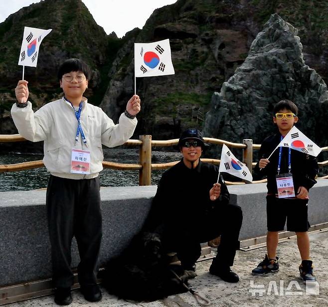 [서울=뉴시스] '2025 독도탐방' 참가자들이 독도경비대 대원과 독도 마스코트인 삽살개와 기념사진을 찍는 모습.