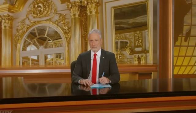 ABC의 ‘데일리 쇼’ 호스트 존 스튜어트가 도널드 트럼프 대통령의 마러라고 별장을 연상시키는 금색 세트에서 트럼프 대통령이 즐겨 입는 빨간색 넥타이를 매고 정장을 입으면서 행정명령에 서명하는 흉내를 내고 있다.  데일리쇼 유튜브 캡처