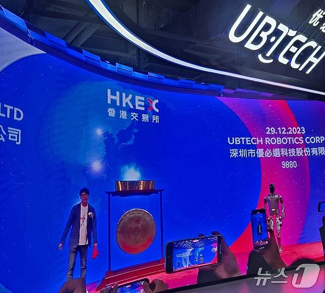유비테크 창업자 저우젠이 2023년 말 홍콩증권거래소 상장 행사에 자사 휴머노이드 로봇과 함께 징을 치기 위해 준비하고 있는 모습.