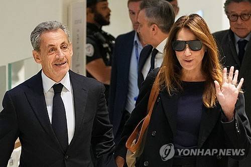 25일 법원 선고 공판에 웃으며 참석하는 니콜라 사르코지 부부 [AP 연합뉴스 자료사진. 재판매 및 DB 금지]