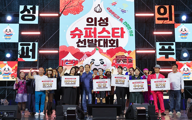 ▲ 28일 경북 의성군 남대천 구봉공원 메인무대에서 열린 제8회 의성슈퍼푸드 마늘축제 '의성 슈퍼스타 선발대회' 시상식에서 김주수 의성군수(가운데)와 대상에 오른 가음면 '아름소리 난타' 팀(회장 신말숙·오른쪽)이 다른 수상자들과 함께 상금 현판을 들고 기념촬영을 하고 있다. 의성군
