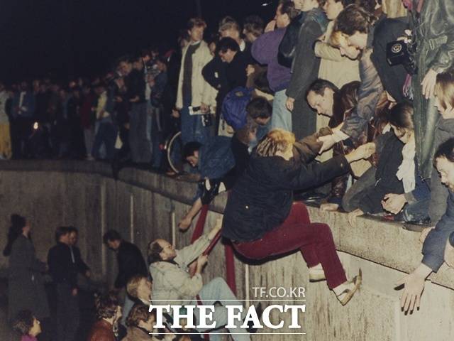 2025년 10월 3일로 독일은 통일 35주년을 맞았지만, 한반도는 여전히 분단된 상태다. 전문가들은 대북 정책의 일관성이 무엇보다 중요하다고 제언했다. 사진은 지난 1989년 11월 10일 동독 동베를린 브란덴부르크 문 근처에서 주민들이 베를린 장벽을 오르며 서독 서베를린 주민들의 도움을 받는 모습. /AP.뉴시스