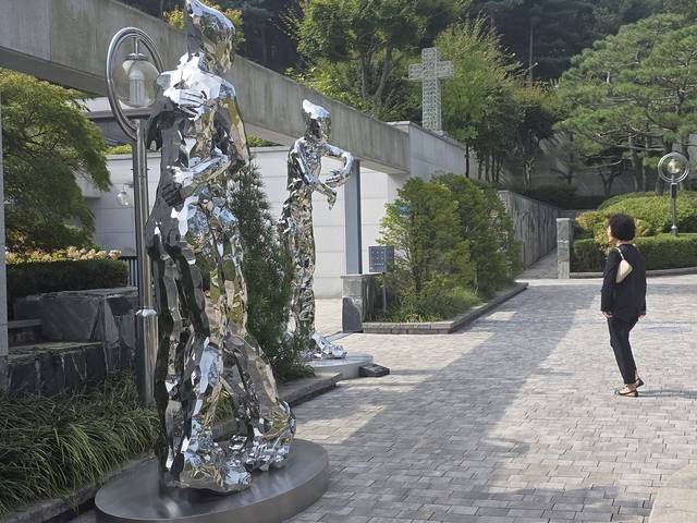 크리스찬메모리얼파크 야외 공간에 설치된 김성복 (성신여대 교수) 작가의 작품 ‘포용’(왼쪽, 195x120x300cm, 스테인리스 스틸)과 ‘사랑은 그리움을 남기고 떠나갔다’(250×120×300cm, 스테인리스 스틸)를 한 추모객이 살펴보고 있다. 크리스찬메모리얼파크 제공