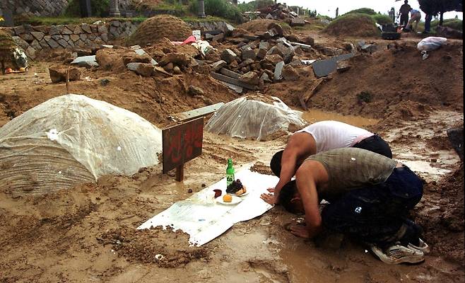 태풍 루사에 따른 폭우로 묘 700여 기가 유실된 강원 강릉시 사천면 석교리 강릉 공원묘지를 찾은 성묘객이 추석에 비를 맞으며 조상 묘에 차례를 지내고 있다. 연합뉴스 제공