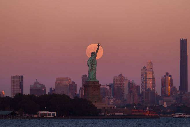 6일(현지 시간) 미 뉴저지주 저지시티에서 자유의 여신상과 브루클린 스카이라인 뒤로 슈퍼문이 떠오르고 있다.  AP 연합