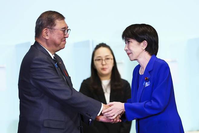 Newly elected Liberal Democratic Party (LDP) leader Sanae Takaichi (right) shakes hands with Prime Minister Shigeru Ishiba after winning the party leadership election at LDP headquarters in Tokyo on October 4. / Xinhua-Yonhap