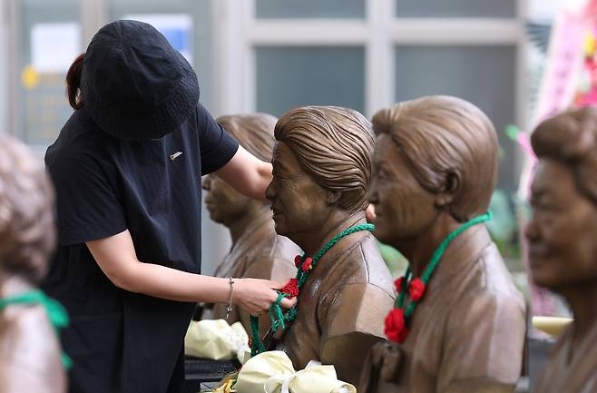 '일본군 위안부 피해자 기림의 날'인 지난 8월 14일 경기 광주시 퇴촌면 나눔의집에서 한 시민이 위안부 피해자 할머니들의 흉상에 직접 뜨개질한 동백꽃 목걸이를 걸고 있다. 뉴스1