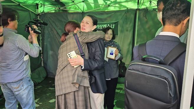 15일 서울 마포구 MBC 사옥 앞에 설치된 고 오요안나씨 분향소에서 어머니 장연미씨가 투쟁에 함께한 시민과 포옹을 하고 있다. 그 뒤에서 김미숙 김용균재단 이사장이 오씨의 명예사원증을 들고 있다. /박지은 기자