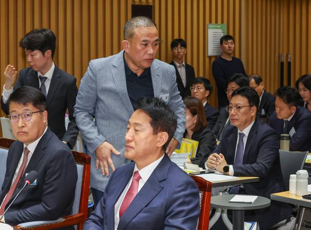 명태균씨가 23일 서울 중구 서울시청에서 열린 2025년 국회 행정안전위원회 국정감사에서 증인석으로 향하며 오세훈 서울시장 뒤로 지나가고 있다. [연합뉴스]