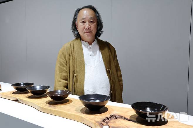 [포항=뉴시스] 박진희 기자 = K-헤리티지 아트전 '이음의 변주‘ 참여작가 김대철 명인이 23일 경북 포항시 문화예술팩토리 아트갤러리에서 전시중이 '목엽천목사발' 작품 앞에서 포즈를 취하고 있다. 2025.10.23. pak7130@newsis.com