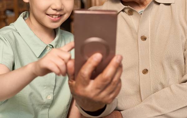 ▲한 어린이가 성인으로 보이는 사람과 나란히 앉아, 성인이 들고 있는 스마트폰 화면을 손가락으로 가리키고 있는 모습으로 연출된 이미지. 사진=Getty Images Bank