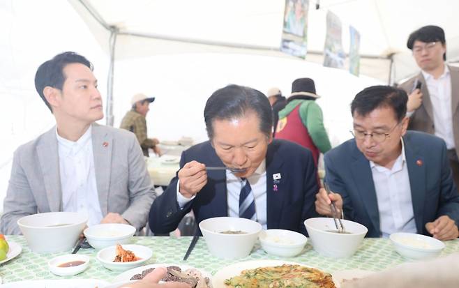 정청래 더불어민주당 대표(가운데)가 25일 제주시 애월읍 새별오름 열린 '2025 제주 도새기 축제'에서 제주 전통 음식인 몸국을 먹고 있다. 왼쪽은 김한규 국회의원(제주시을), 오른쪽은 위성곤 국회의원(서귀포시) / 연합뉴스