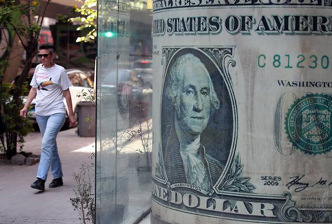 한 여성이 대형 미국 달러 지폐 이미지를 지나가고 있다. /연합뉴스