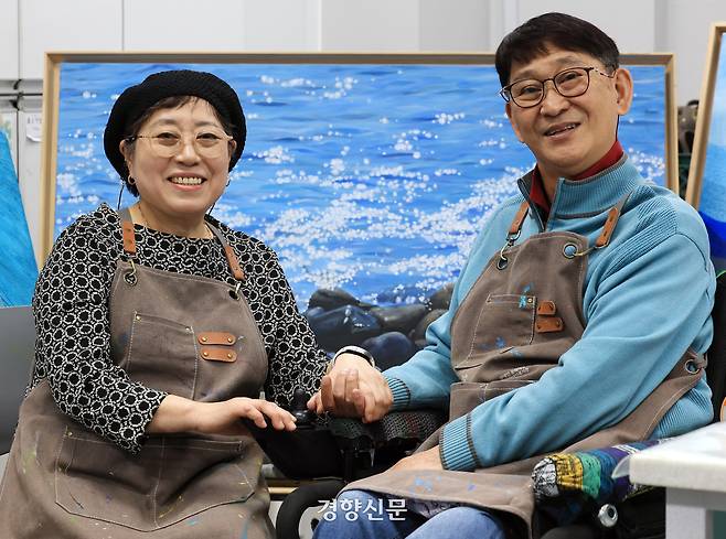 문정연 이병륜 부부가 24일 서울 강남장애인복지관 내 작업실에서 손을 마주잡고 포즈를 취하고 있다. 배경에 등장한 작품은 문 작가가 위안을 받았던 거제도의 바다를 담은 그림이다. 서성일 선임기자